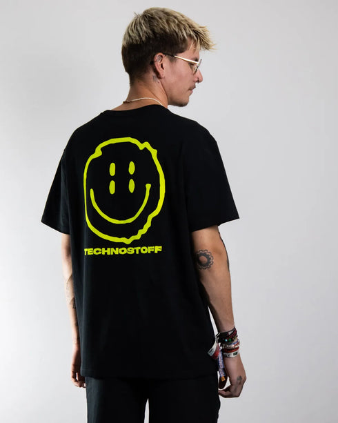 Schwarzes "Distorted Smile" oversized T-Shirt mit neon gelben Smily-Flockdruck auf dem Rücken, getragen von einem Mann, fotografiert von hinten