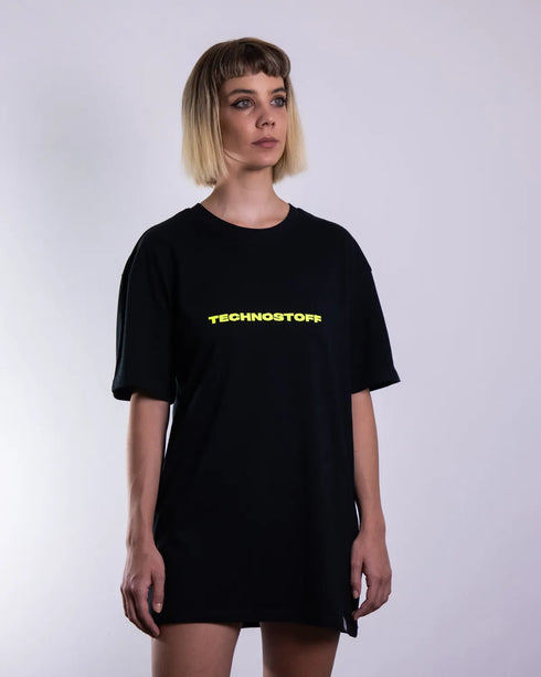 "NYS" oversized T-Shirt für Raver in schwarz mit neon gelbem Technostoff Schriftzug, getragen von einer Frau, von vorne fotografiert