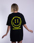 Schwarzes "Distorted Smile" oversized T-Shirt mit neon gelben Smily-Flockdruck auf dem Rücken, getragen von einer Frau, fotografiert von hinten