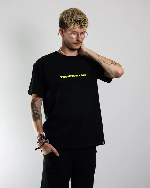 "NYS" oversized T-Shirt für Raver in schwarz mit neon gelbem Technostoff Schriftzug, getragen von einem Mann, von vorne fotografiert