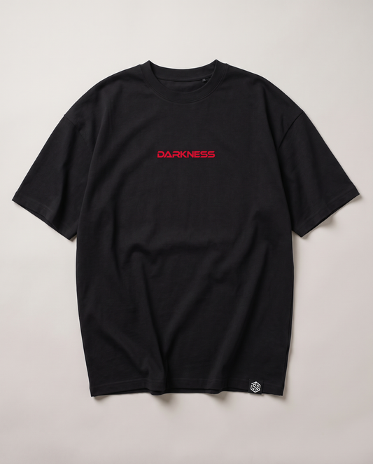 Technostoff DARKNESS T-Shirt in Schwarz, oversized, mit rotem gesticktem DARKNESS-Schriftzug mittig auf der Brust und kleinem gewebtem Label am Saum, Flatlay Vorderseite auf hellem Hintergrund