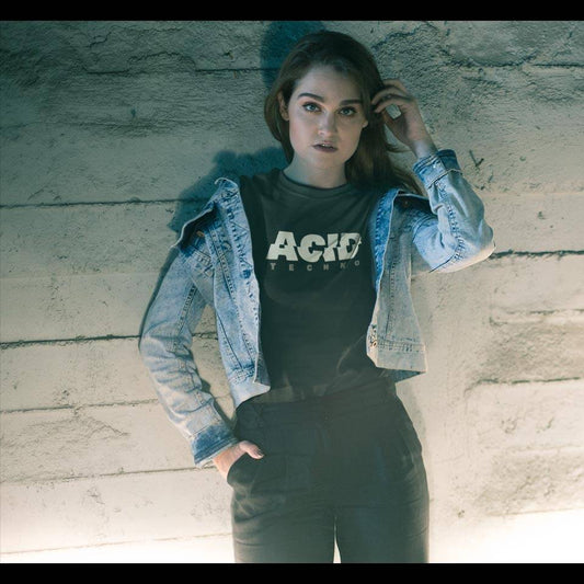 Junge Raverin mit Jeansjacke lehnt an Betonwand und trägt das schwarze Technostoff Acid Techno T-Shirt