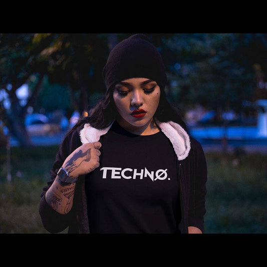 Tattooed female raver with beanie and red lipstick wearing the black Technostoff New Techno T-shirt in the evening in a park