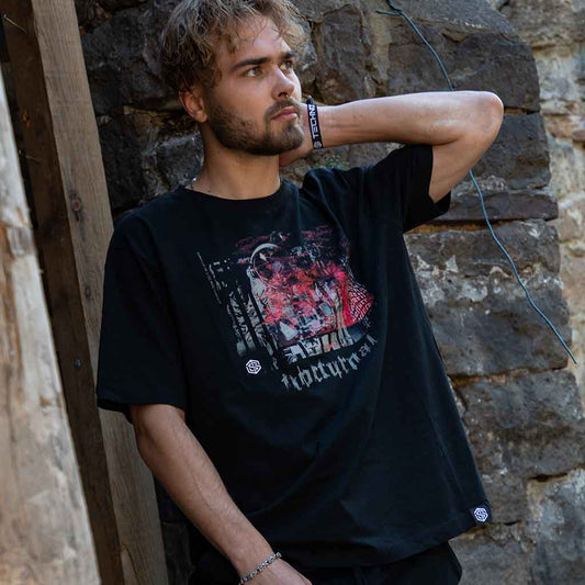 Raver leaning against stone wall in the black Technostoff Nocturnal Astronaut oversized T-shirt with red glitch print
